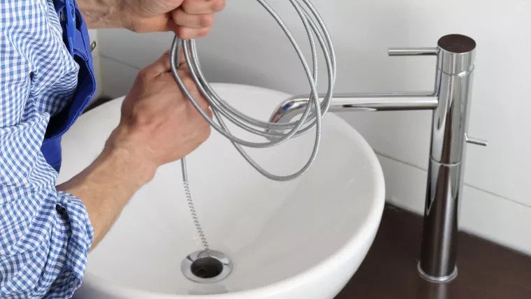 Plumber Unclogging Sink Using Wire